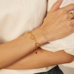 Close-up of a gold stainless steel chain bracelet with four hollow heart pendants