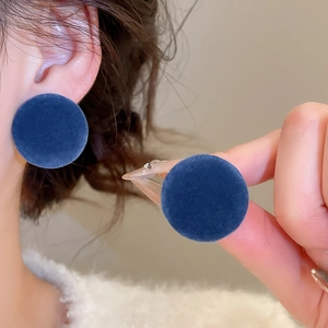 Close-up of deep blue flocked round stud earring on ear showing soft velvet texture