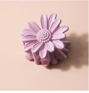 Detailed top view of a small purple daisy hair claw clip on a soft nude background