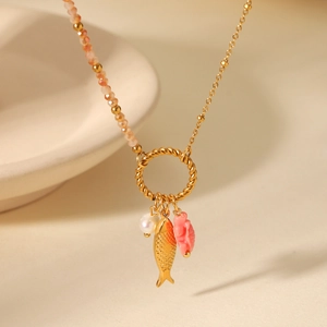 Golden titanium steel necklace with sea turtle fish charms and pink beads on a white bowl