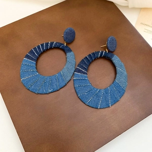 Detail of blue denim fabric patchwork earrings with decorative stitching on leather base