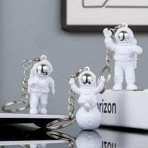 Three white astronaut keychains set with silver visors in standing and sitting poses