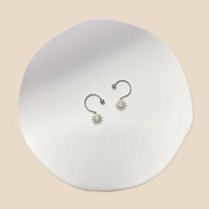 Detail of silver sun-pendant earrings with small crystals on a white ceramic plate