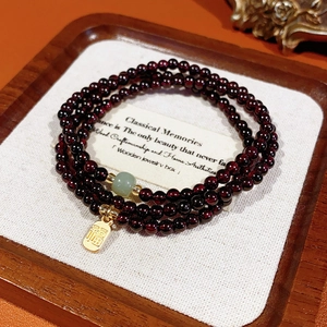 Macro detail of garnet beads with a jade accent and a gold Fu character charm on a tray