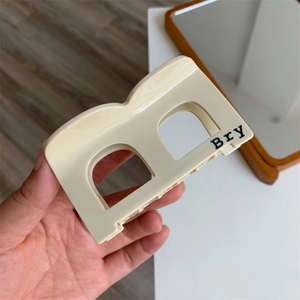 Detail view of a beige acetate hair claw clip with cutout design and Bry lettering