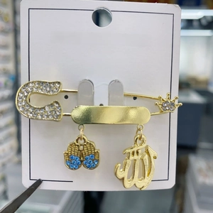 Detail of a gold pin brooch with blue Hand of Fatima and Arabic charms on fashion card