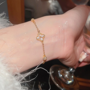 Close-up of gold clover bracelet with zircon flowers and pearls on woman wrist