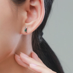 Cute S925 sterling silver dinosaur stud earrings with green crystal on a model's ear