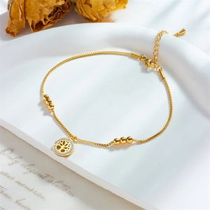 Elegant gold titanium Tree of Life anklet with crystal inlay and bead chain on white tray