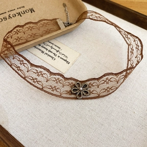 Detail of brown lace choker with rhinestone flower pendant and pearl on white fabric