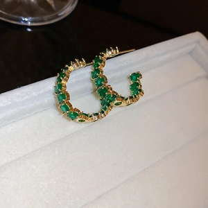 Dettaglio di orecchini a cerchio dorati con cristalli rotondi verde smeraldo su velluto