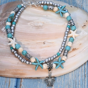 Detail of a layered ocean-style anklet with silver sea turtle and blue starfish charms