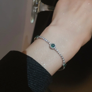 Detail of elegant silver bow bracelet featuring sparkling green stones and tennis chain