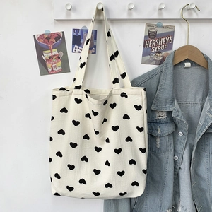 Close-up of white heart print canvas tote bag hanging on wooden hook with vintage posters