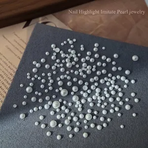 Mix of flatback faux pearl nail art gems in various sizes on a textured gray block