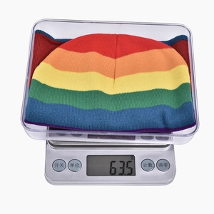 Rainbow striped knit beanie weighing 63.5g displayed on a precision digital scale