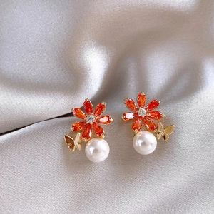 Détail de boucles d'oreilles fleur avec pierres oranges, perle et papillon sur soie