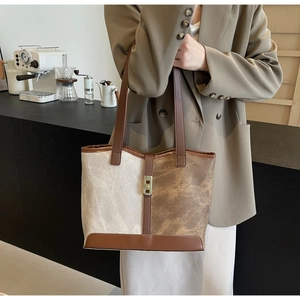 Close-up of a two-tone tote bag with a golden metal lock and brown leather handles