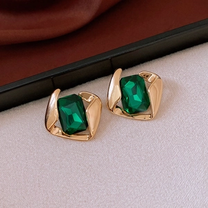 Close-up of vintage emerald-style stud earrings with gold plating on beige background