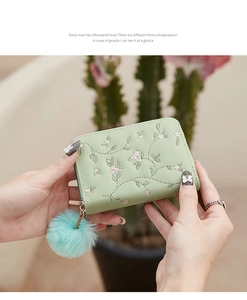 Detail of light green faux leather wallet with floral embroidery and soft pompom charm