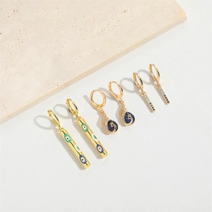 Three pairs of gold drop earrings featuring evil eye and heart patterns on stone tray