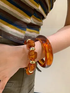 Detail of amber acrylic resin geometric bracelet and beaded bangle on female wrist