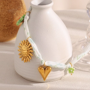 Pendentifs soleil et cœur dorés 18K sur un collier en corde verte sur un vase blanc