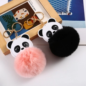 Close-up of plush panda pompom keychains with pink and black fur balls and gold hardware