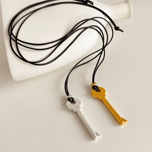 Détail de pendentifs clés en argent et or sur cordons en cuir avec un fond blanc épuré