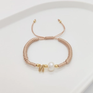 Detail of handmade woven bracelet with freshwater pearl and golden letter N charm