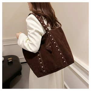 Close-up of brown tote bag featuring silver studs on straps and a heart pendant