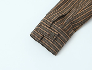 Close-up of brown plaid cotton shirt cuff with a dark button and neat stitching details