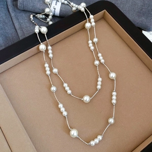Close-up of double-layer faux pearl necklace with silver chain on premium textured fabric