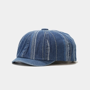 Macro detail of dark blue denim newsboy cap with vertical striped stitching and cotton texture