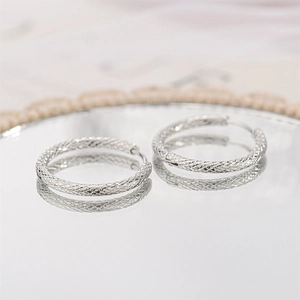 Macro detail of silver hoop earrings with woven mesh texture on reflective mirror surface