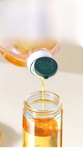 Close-up of pouring oil into wide-mouth glass kitchen bottle with green lid