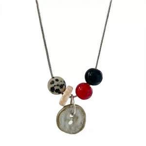 Macro detail of spotted stone beads and vintage button pendant on silver snake chain