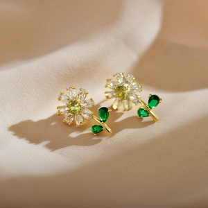 Macro detail of gold-plated floral earrings with green crystals on beige fabric