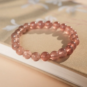 Detailed view of pink strawberry quartz bracelet beads with natural inclusions on a book