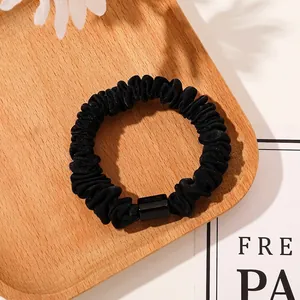 Detailed shot of black satin scrunchie with glossy buckle on light wood tray