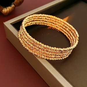 Detailed view of multilayer gold-plated spiral bangle resting on a luxury jewelry box