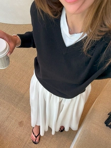 Top-down view of a woman wearing a white pleated skirt and a black V-neck knitted sweater