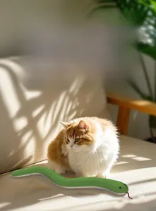 Detail of green knitted catnip snake toy being played with by a ginger and white cat