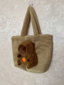 Detail of Capybara plush backpack hanging on hook showing soft khaki fabric and 3D doll