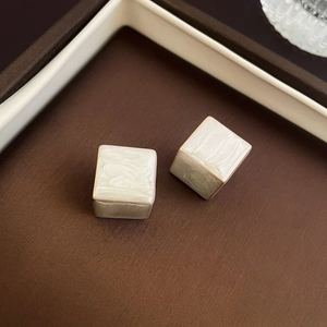 Detailed close-up of square pearl earrings with silver base on a textured surface