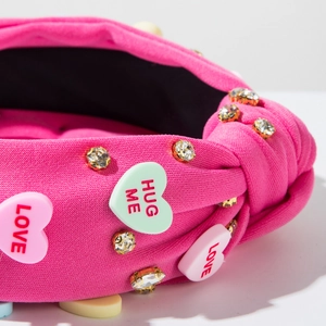 Close-up of pink headband with rhinestones and heart charms featuring LOVE and HUG ME text