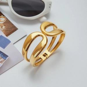 Polished gold stainless steel bangle featuring a double hollow arc crossed design on white