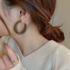 Close-up of olive green C-shaped resin hoop earrings worn by a model in white knitwear