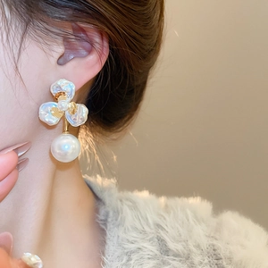 Close-up of elegant flower petal pearl earrings worn by a model in soft indoor lighting