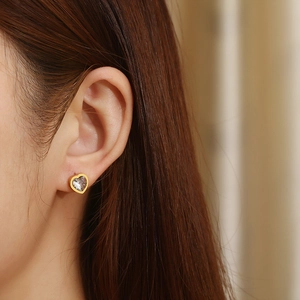 Close-up of gold heart stud earring with clear crystal on female model ear